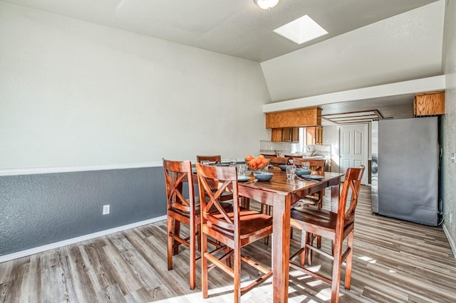 dining space with vaulted ceiling with skylight, light wood-style flooring, and baseboards