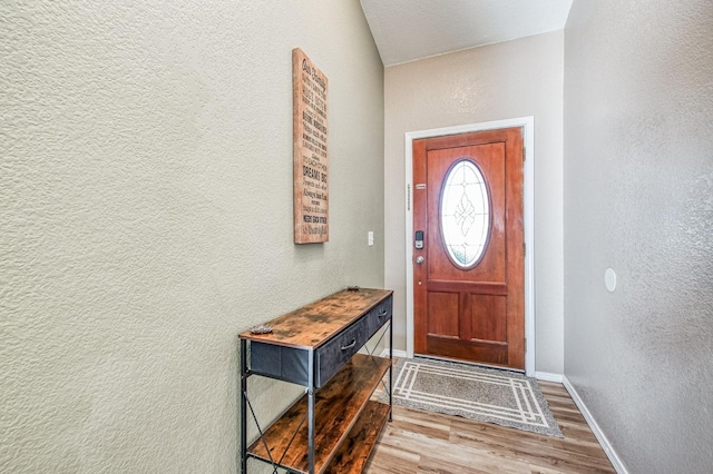 doorway featuring a textured wall, wood finished floors, and baseboards