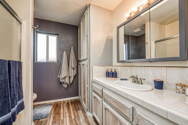 full bath with a textured wall, backsplash, wood finished floors, and vanity