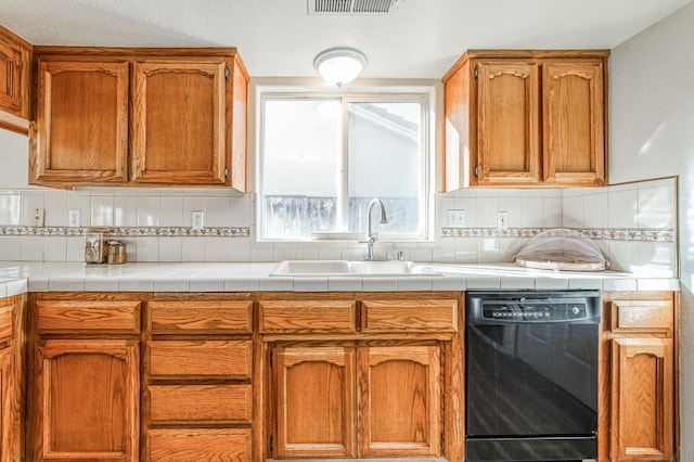 kitchen featuring black dishwasher, brown cabinetry, tile countertops, a sink, and backsplash