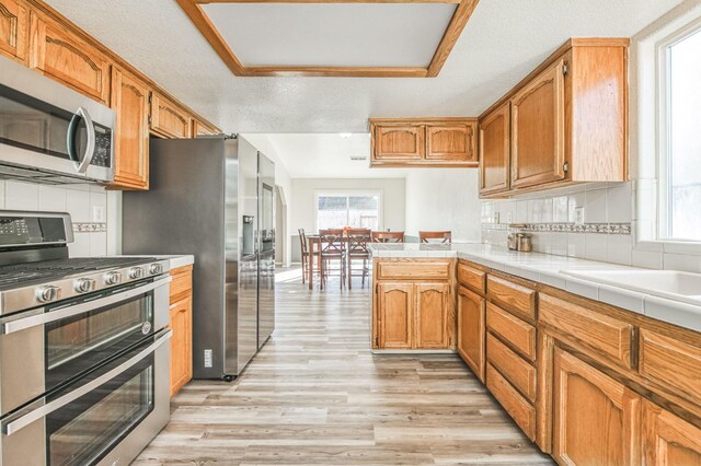 kitchen featuring appliances with stainless steel finishes, light hardwood / wood-style floors, backsplash, and tile counters