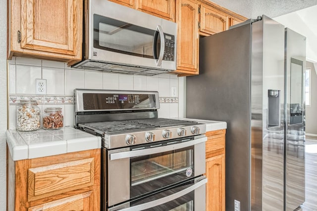 kitchen with stainless steel appliances, tile countertops, and tasteful backsplash