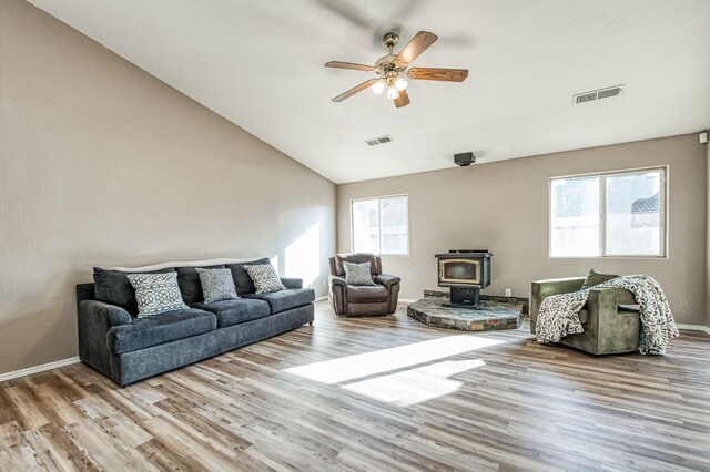 living room featuring light hardwood / wood-style floors, ceiling fan, vaulted ceiling, and a wood stove