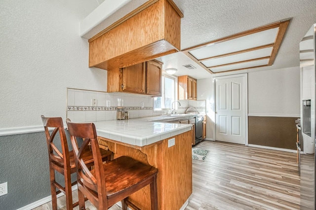 kitchen featuring brown cabinetry, tile countertops, a kitchen breakfast bar, a peninsula, and a sink