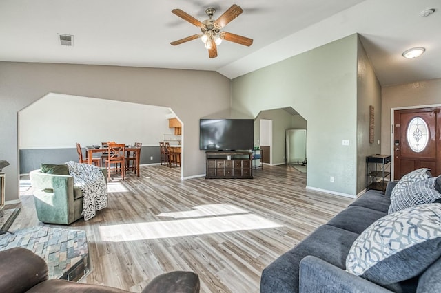 living room featuring arched walkways, light wood finished floors, visible vents, a ceiling fan, and vaulted ceiling