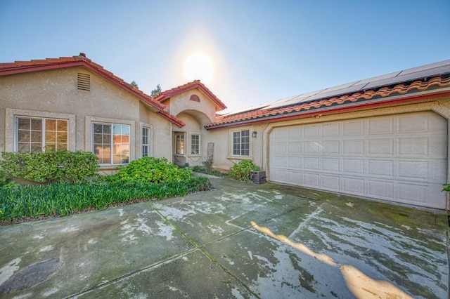 view of front facade featuring stucco siding, solar panels, an attached garage, driveway, and a tiled roof