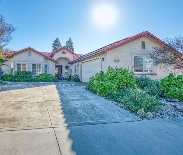 mediterranean / spanish-style home featuring a garage, concrete driveway, a tiled roof, and stucco siding