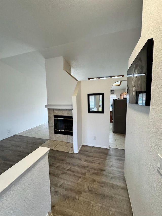 unfurnished living room featuring arched walkways, wood finished floors, and a tile fireplace