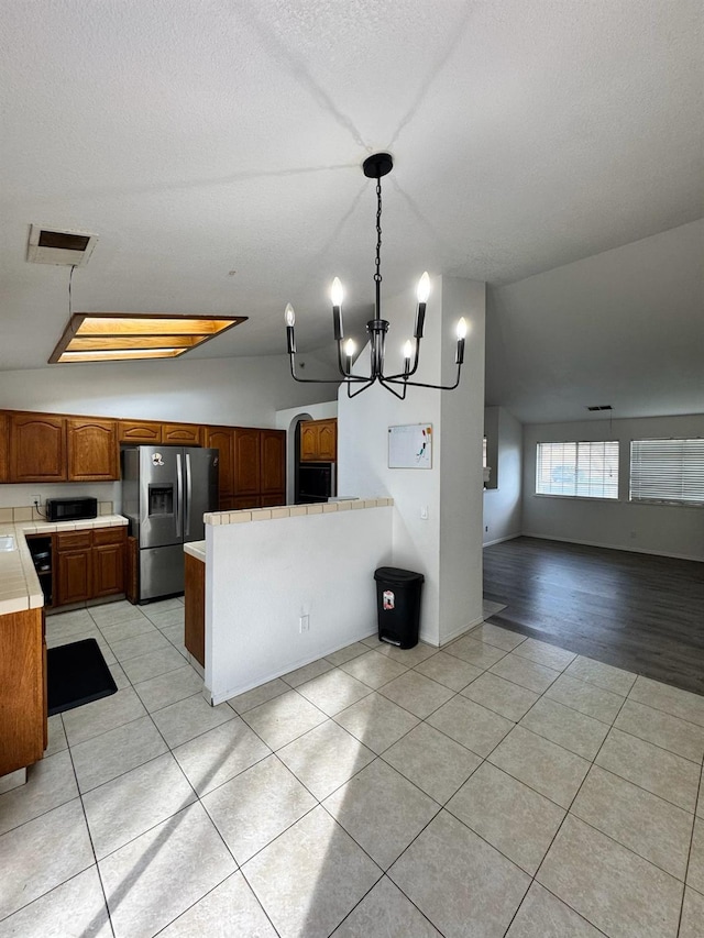 kitchen with light tile patterned floors, stainless steel fridge, open floor plan, a peninsula, and black microwave