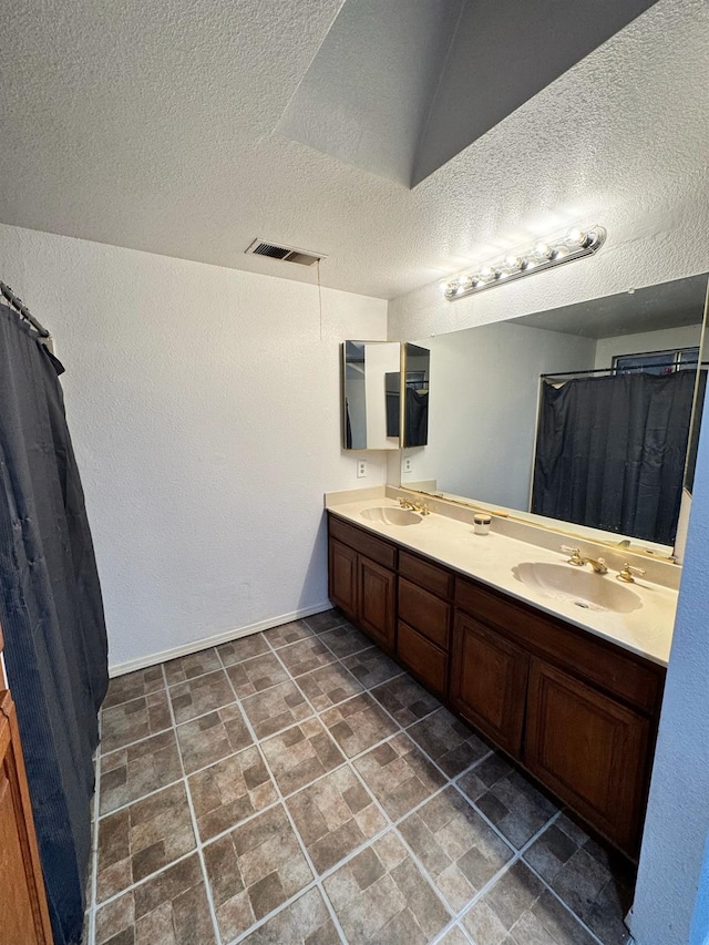 bathroom with a textured ceiling, double vanity, a sink, and visible vents