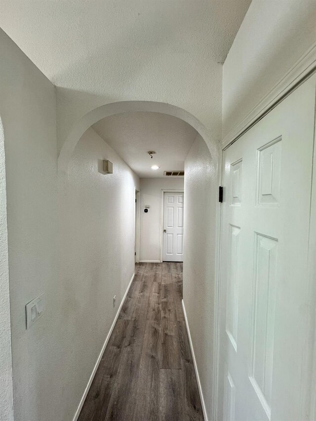 hall with arched walkways, a textured ceiling, visible vents, baseboards, and dark wood-style floors