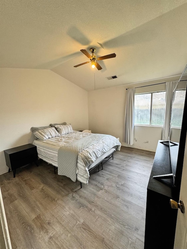 bedroom with visible vents, a ceiling fan, wood finished floors, vaulted ceiling, and a textured ceiling