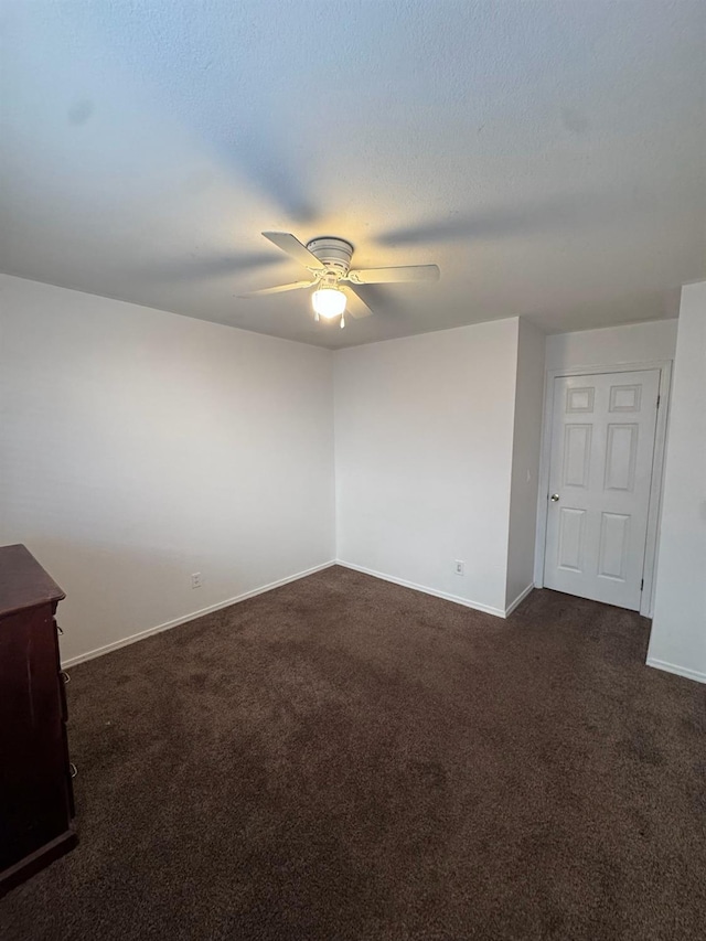 unfurnished room featuring a textured ceiling, dark colored carpet, a ceiling fan, and baseboards