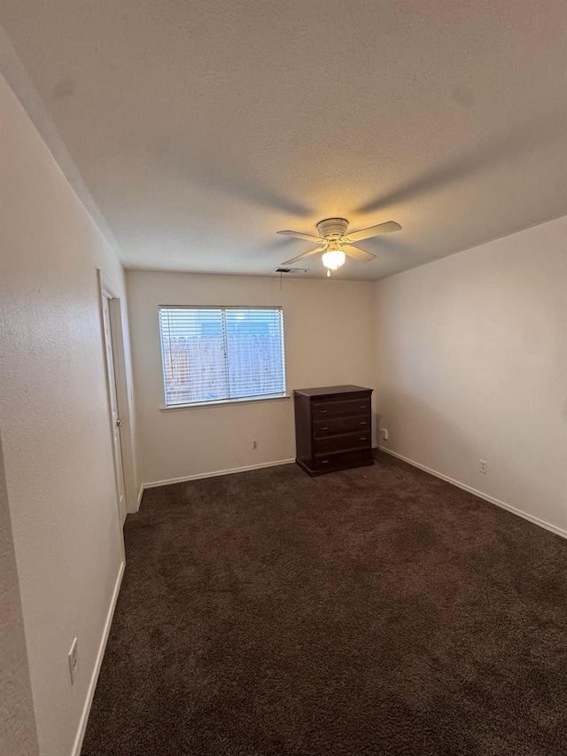 empty room with a ceiling fan, baseboards, dark carpet, and a textured ceiling