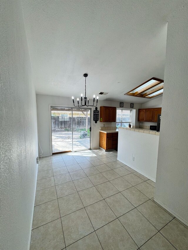 unfurnished dining area with an inviting chandelier, light tile patterned flooring, a textured ceiling, and a textured wall