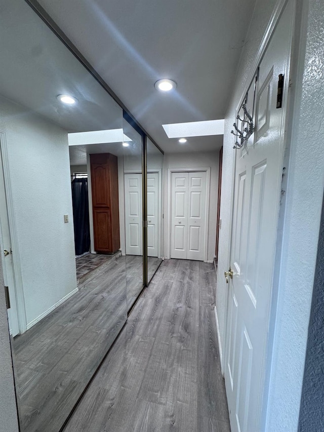 hall featuring a skylight, baseboards, a textured wall, wood finished floors, and recessed lighting