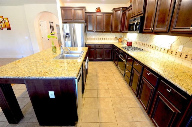 kitchen with backsplash, a center island with sink, sink, stainless steel appliances, and light tile patterned floors