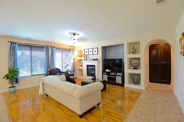 tiled living room with ceiling fan and built in features