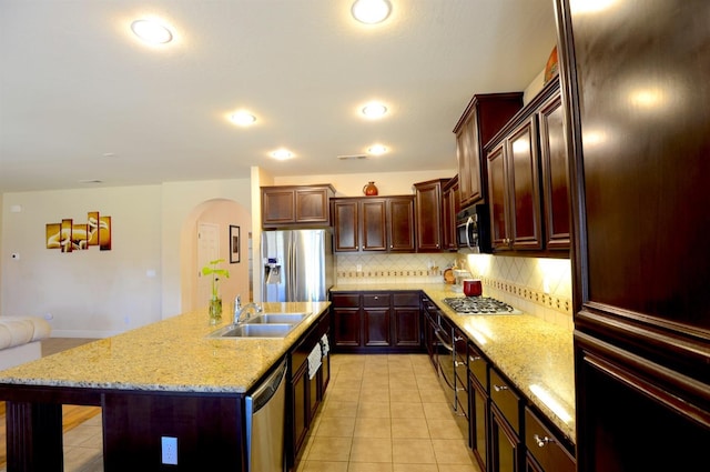 kitchen featuring light stone countertops, stainless steel appliances, an island with sink, decorative backsplash, and sink