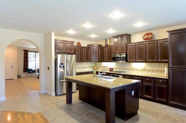 kitchen featuring a center island with sink, appliances with stainless steel finishes, light stone counters, a breakfast bar, and sink