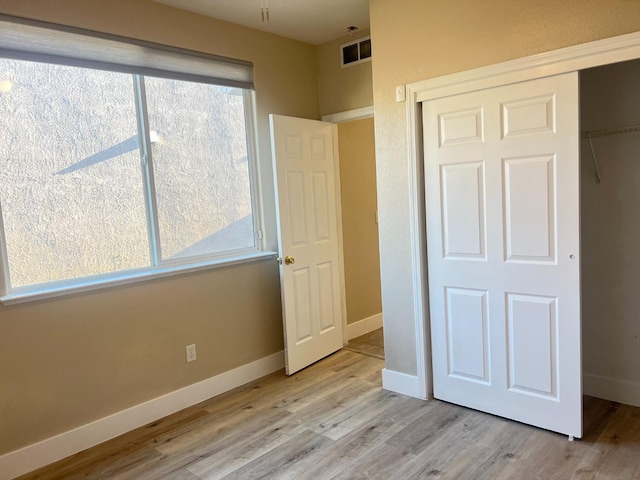 unfurnished bedroom featuring a closet, light hardwood / wood-style flooring, and multiple windows