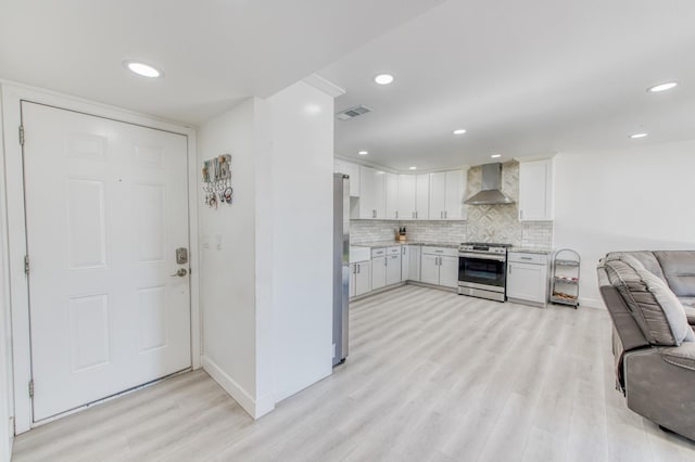 kitchen with white cabinets, appliances with stainless steel finishes, wall chimney range hood, and light hardwood / wood-style floors