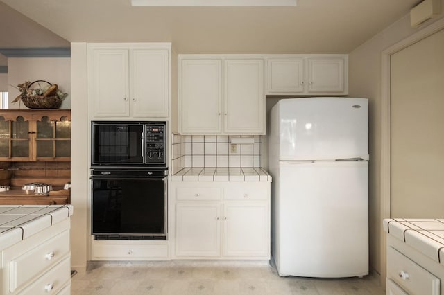 kitchen with tasteful backsplash, white cabinets, tile countertops, and black appliances