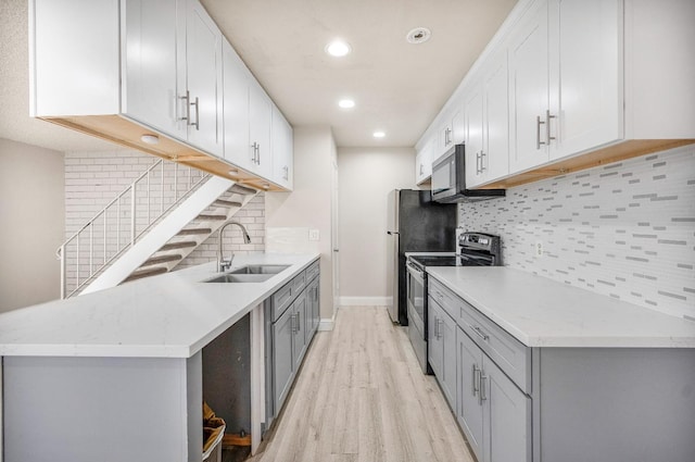 kitchen featuring appliances with stainless steel finishes, sink, white cabinets, light hardwood / wood-style flooring, and tasteful backsplash