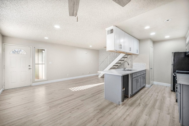 kitchen with gray cabinetry, a textured ceiling, white cabinets, light hardwood / wood-style flooring, and tasteful backsplash