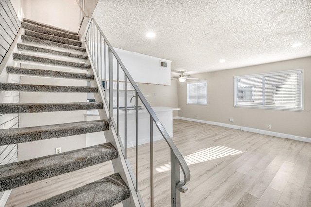 stairway with hardwood / wood-style floors, a textured ceiling, and ceiling fan