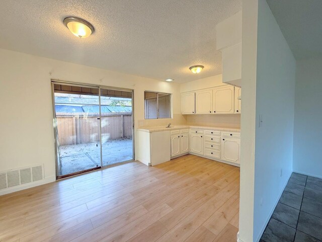 kitchen featuring sink, white cabinetry, a textured ceiling, and light hardwood / wood-style flooring