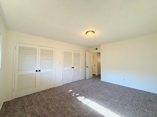 unfurnished bedroom featuring carpet floors, a textured ceiling, and multiple closets