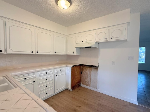 kitchen with white cabinets, a textured ceiling, tile countertops, tasteful backsplash, and light hardwood / wood-style flooring