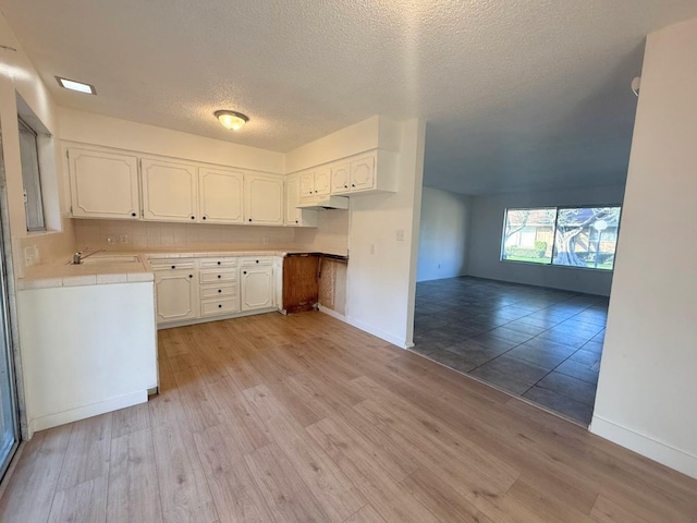 kitchen featuring a textured ceiling, tile countertops, light hardwood / wood-style flooring, white cabinets, and sink