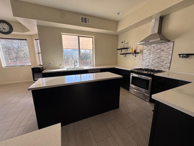 kitchen with a center island, stainless steel range with gas cooktop, wall chimney exhaust hood, sink, and backsplash