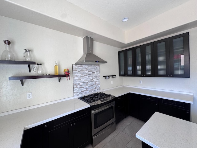 kitchen featuring gas range, wall chimney range hood, light tile patterned floors, and decorative backsplash