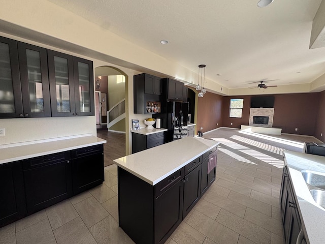 kitchen featuring decorative light fixtures, black refrigerator with ice dispenser, a kitchen island, a fireplace, and ceiling fan