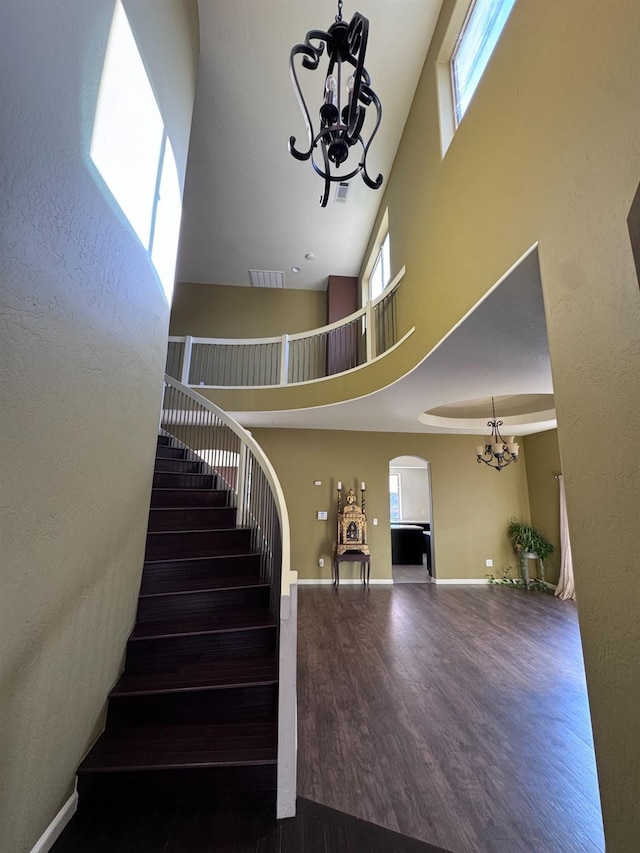 stairway featuring a towering ceiling, hardwood / wood-style flooring, and a notable chandelier