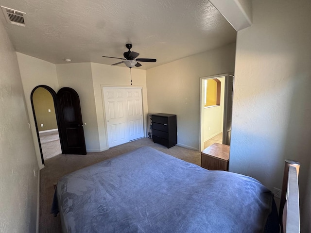 bedroom featuring ceiling fan, light colored carpet, a closet, and a textured ceiling