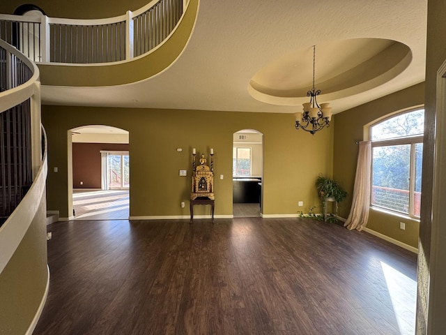 empty room featuring a raised ceiling, an inviting chandelier, a wealth of natural light, and dark hardwood / wood-style floors