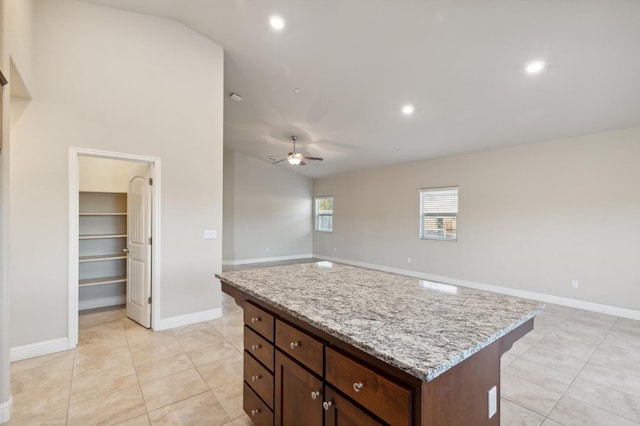 kitchen with ceiling fan, light stone countertops, a kitchen island, and light tile patterned floors