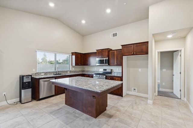 kitchen featuring appliances with stainless steel finishes, light tile patterned flooring, light stone counters, and a kitchen island