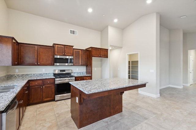 kitchen with sink, a center island, light stone counters, a high ceiling, and appliances with stainless steel finishes