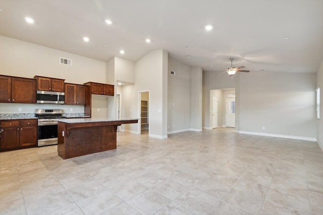 kitchen with appliances with stainless steel finishes, a center island, a towering ceiling, ceiling fan, and light stone counters