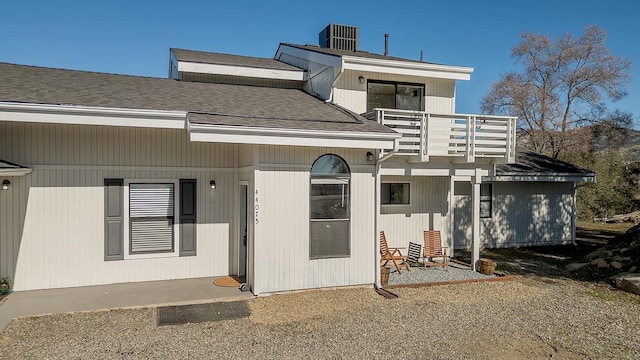 back of house featuring a balcony, central air condition unit, and roof with shingles