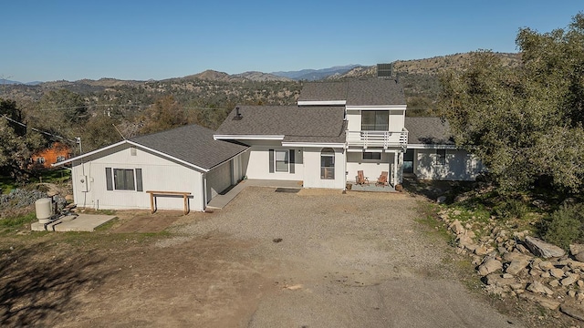 view of front of house featuring a mountain view, a patio, a shingled roof, and a balcony