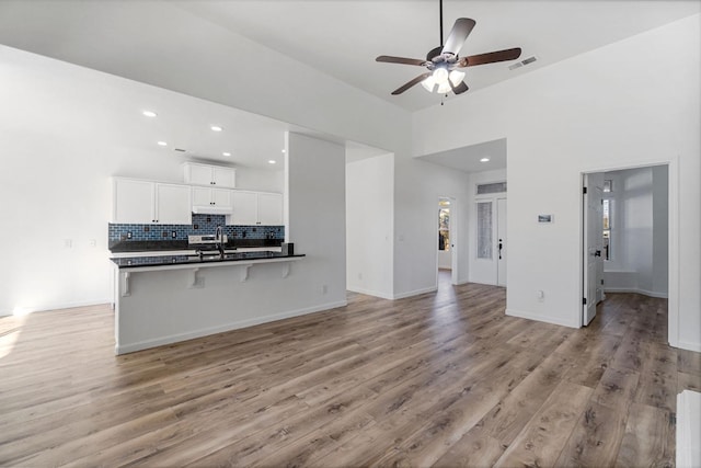 kitchen featuring white cabinetry, kitchen peninsula, ceiling fan, light hardwood / wood-style flooring, and a breakfast bar area