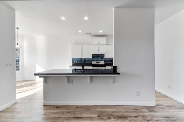 kitchen with white cabinets, sink, backsplash, stainless steel range with electric stovetop, and a breakfast bar area