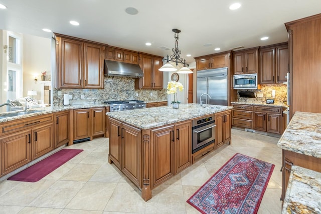 kitchen with a kitchen island, decorative light fixtures, built in appliances, tasteful backsplash, and sink