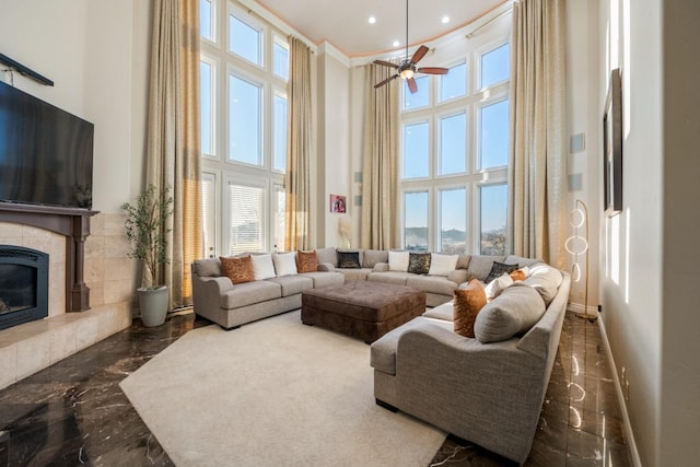 living room with ceiling fan, plenty of natural light, a tile fireplace, and a towering ceiling